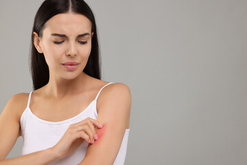 Fototapeta premium Suffering from allergy. Young woman scratching her arm on light grey background. Space for text