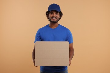 Happy young courier with parcel on light brown background