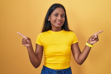 Young indian woman standing over yellow background smiling confident pointing with fingers to different directions. copy space for advertisement