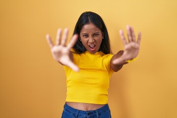 Obraz premium Young indian woman standing over yellow background doing stop gesture with hands palms, angry and frustration expression