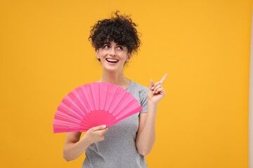 Happy woman holding hand fan on orange background. Space for text - obrazy, fototapety, plakaty