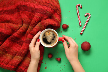 Female hands with red manicure, cup of coffee, knitted scarf and Christmas decor on green background