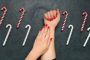 Female hands with red manicure and Christmas candy canes on black grunge background