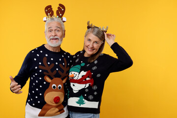 Senior couple in Christmas sweaters and reindeer headbands on orange background. Space for text