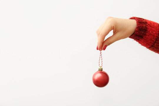 Female hand with red manicure holding Christmas ball on white background, closeup