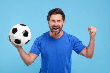 Emotional sports fan with soccer ball on light blue background