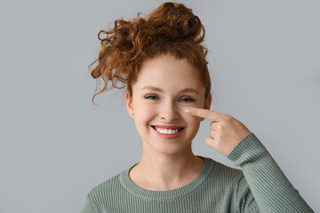 Portrait of pretty young girl pointing at her nose on grey background