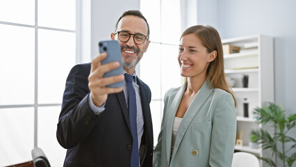 Two business workers standing together having video call by smartphone at office