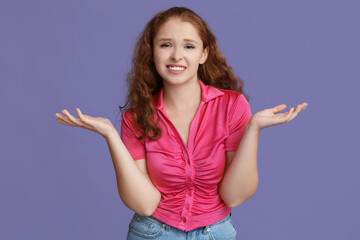 Portrait of ashamed young woman shrugging on purple background