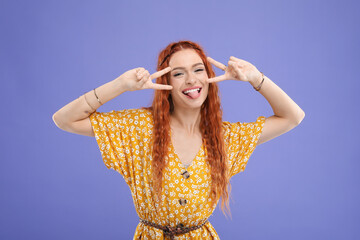 Beautiful young hippie woman showing V-sign on violet background
