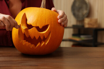 Woman carving pumpkin for Halloween at wooden table indoors, closeup