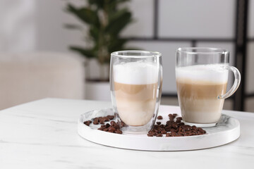 Aromatic latte macchiato and coffee beans on white marble table against blurred background. Space for text