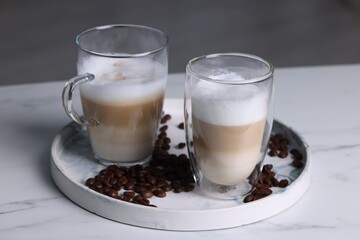 Aromatic latte macchiato and coffee beans on white marble table against blurred background, closeup