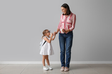 Beautiful mother and her cute little daughter with cups of tea near grey wall