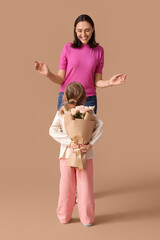 Cute little daughter greeting her beautiful mother with bouquet of roses on brown background. Happy...