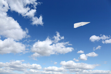 Naklejka na ściany i meble White paper plane flying in blue sky with clouds