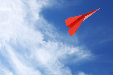 Fototapeta na wymiar Red paper plane flying in blue sky with clouds