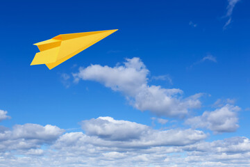 Yellow paper plane flying in blue sky with clouds