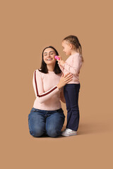 Beautiful mother and her cute little daughter doing makeup on brown background