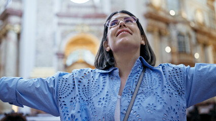 Fototapeta premium Young beautiful hispanic woman visiting church with open arms at St. Karl BorromÃ¤us church