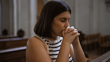 Fototapeta na wymiar Young beautiful hispanic woman praying on a church bench at Augustinian Church in Vienna