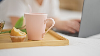 Young beautiful hispanic woman eating cupcake and drinking coffee for breakfast using laptop at bedroom