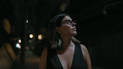 Fototapeta premium Cheerful beautiful hispanic woman in glasses enjoying kyoto's nightlife, looking around and smiling confidently on a lighted japanese street