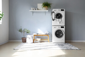 Interior of modern laundry room with washing machines and grey bench