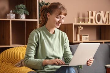 Fototapeta premium Young woman using laptop on sofa at home