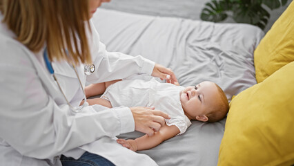 Fototapeta premium Confident female doctor joyfully examining adorable baby, sitting on bed in cozy bedroom - casual healthcare moment in a loving home environment