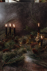 Christmas dark academia vintage winter wooden table with fir branches, pine cones, black candles and twinkle lights covered in fake snow