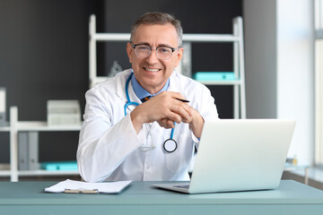 Mature doctor working at table in medical office