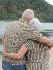 Pareja de jubilados abrazándose de espaldas con río y palmeras al fondo