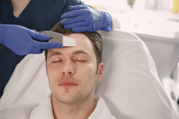 Young man in cosmetologist cabinet has a face procedure of cavitation
