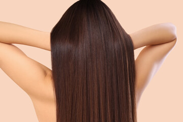 Young brunette woman with beautiful hair on beige background, back view