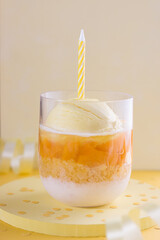 Glass with ice cream, chopped fruit, cake and Greek yogurt with happy birthday decoration.