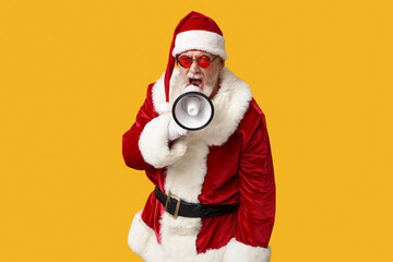 Santa Claus in sunglasses with megaphone screaming on yellow background