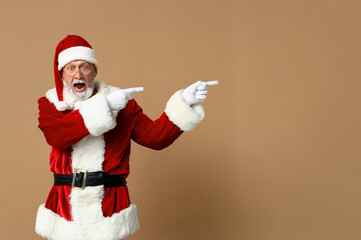 Fototapeta na wymiar Shocked Santa Claus in glasses pointing at something on brown background