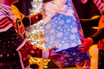 Couple giving each other Christmas gifts in the exchange, in the background you can see the lights of the Christmas tree