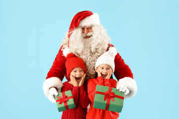 Surprised little children receiving Christmas gifts from Santa Claus on blue background