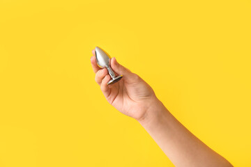 Female hand with anal plug on yellow background, closeup