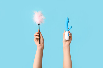 Female hands with vibrator and feather stick from sex shop on color background - obrazy, fototapety, plakaty