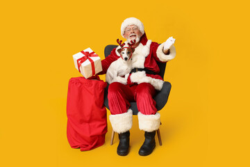 Santa Claus with cute Jack Russell Terrier dog in reindeer horns and bag on yellow background