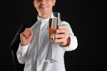 Young man with glass of champagne celebrating Christmas on black background