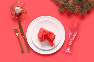 Beautiful table setting with Christmas tree branches, gift box and candle on red background