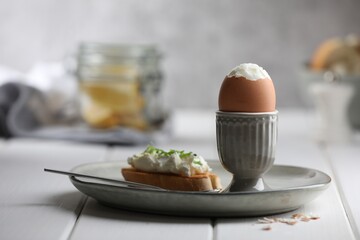 Fresh soft boiled egg in cup and sandwich on white wooden table. Space for text