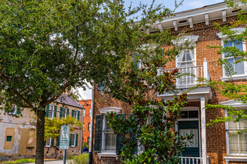 Naklejka premium Charming brick townhouse with green shutters nestled among mature trees in Savannah, Georgia, USA