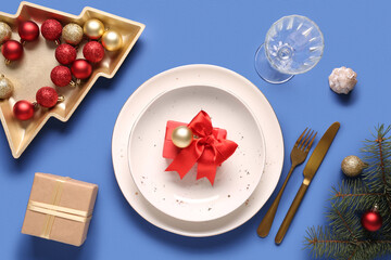 Beautiful table setting with Christmas balls, fir branches and gift box on blue background