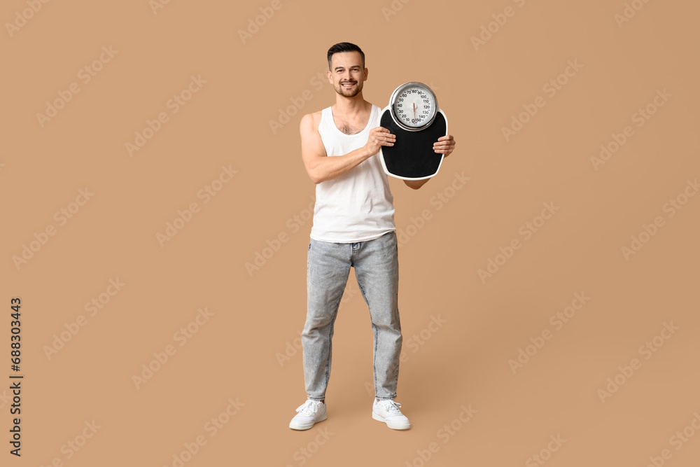 Wall mural Handsome sporty young man with scales on brown background. Weight loss concept