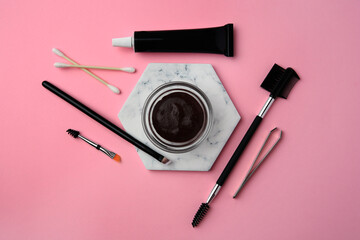 Flat lay composition with eyebrow henna and tools on pink background